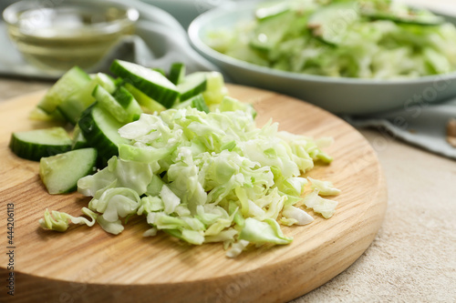 Wooden board with chopped cabbage and cucumber on light table, closeup