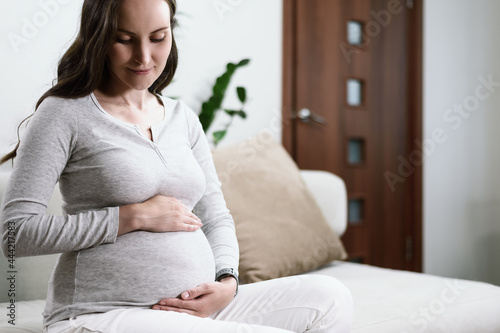 beautiful pregnant woman sitting on couch with hands on pregnant belly, happy pregnancy