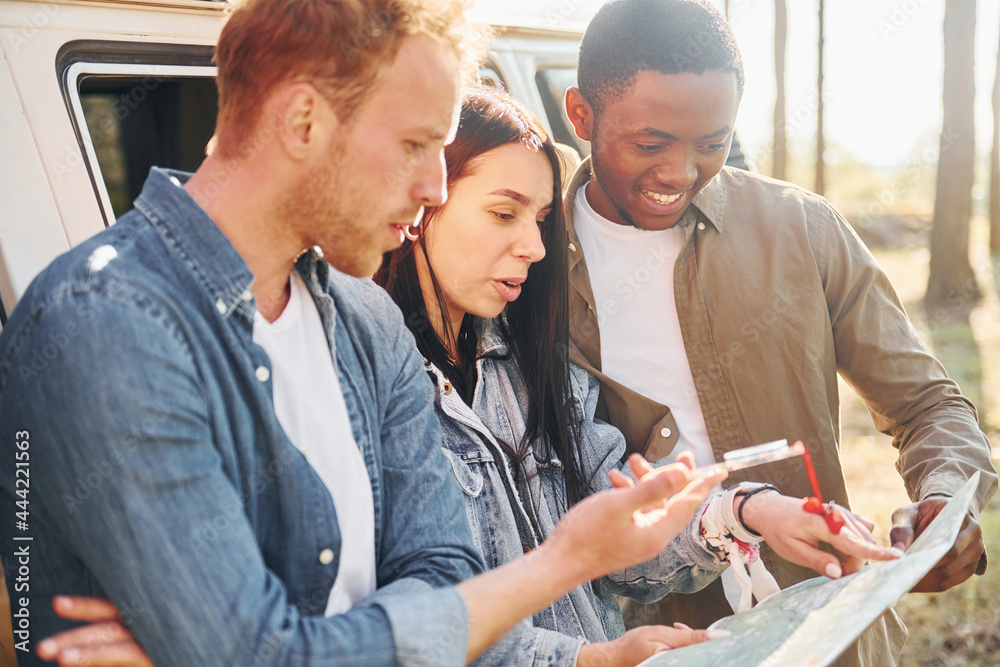 Holding map and looking for location. Group of young people is traveling together in the forest Holding map and looking for location. Group of young people is traveling together in the forest