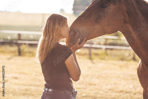 Young mistress in evening on ranch in rays of sunset greets her horse. Concept of love and trust. Active lifestyle. Life in nature . Beauty and health.