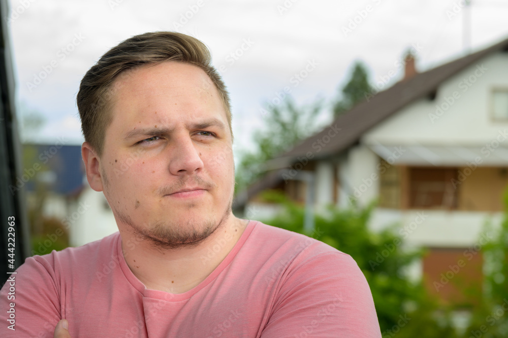Young man sitting outdoors thinking deeply and frowning
