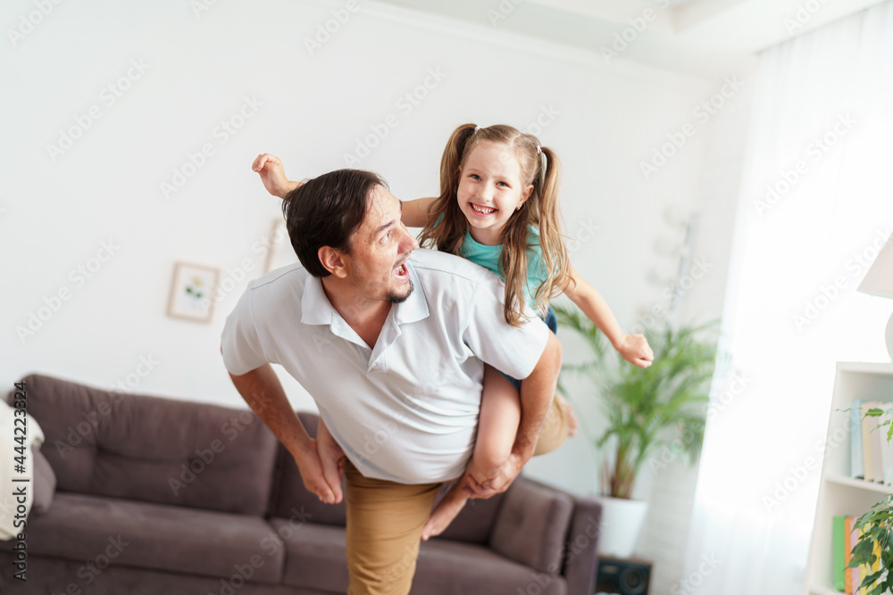 Happy positive cheerful dad is playing with his little charming daughter at home. The man circles and throws the girl up. A dynamic image. Copy space Happy positive cheerful dad is playing with his little charming daughter at home. The man circles and throws the girl up. A dynamic image. Copy space