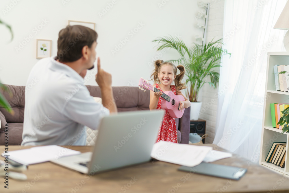 father works at home with laptop together with daughter. little girl wants to play guitar, noise and interfere with work. man shakes his finger at her and asks them to calm down remote work at home father works at home with laptop together with daughter. little girl wants to play guitar, noise and interfere with work. man shakes his finger at her and asks them to calm down remote work at home