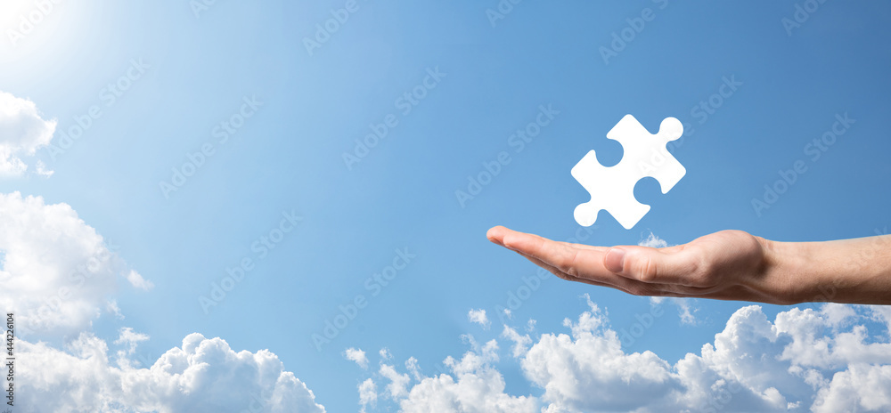 Male hand holding puzzle icon on blue background. pieces representing the merging of two companies or joint venture, partnership, Mergers and acquisition concept. Male hand holding puzzle icon on blue background. pieces representing the merging of two companies or joint venture, partnership, Mergers and acquisition concept.