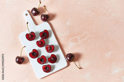 Top view cherry berries are cut into halves and lie on a white ceramic cutboard over pink background with a copyspace. photo