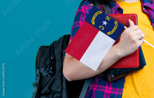 Young girl with school stuff holds in hand North Carolina flag close up