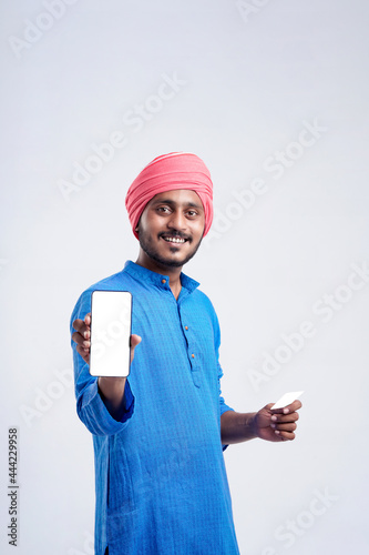 Young indian farmer showing card and smartphone on white background.