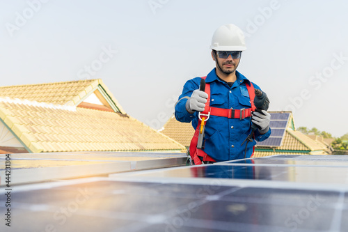 A worker wearing fall protection safety equipment while installing the solar panels at roof top of building. Concept of economic energy. High safety standard working procedure.