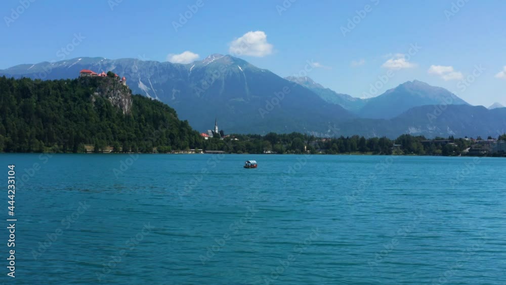 Man Rowing Traditional Boat (Pletna) With Tourists On Lake Bled In Slovenia. Scenic View Of Bled Castle And Beautiful Mountain In Background. wide shot Man Rowing Traditional Boat (Pletna) With Tourists On Lake Bled In Slovenia. Scenic View Of Bled Castle And Beautiful Mountain In Background. wide shot
