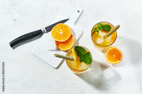 Top view of prepering summer cockteil. Glasses with gin and cold tonic with orange and mint, decorated with slices and with ice cubes on white background and bamboo straw. photo