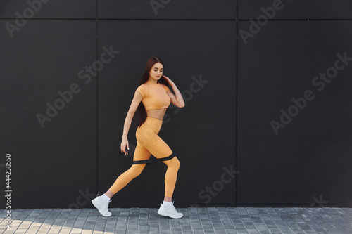 Uses stretching tape. Young woman in sportswear have fitness session outdoors