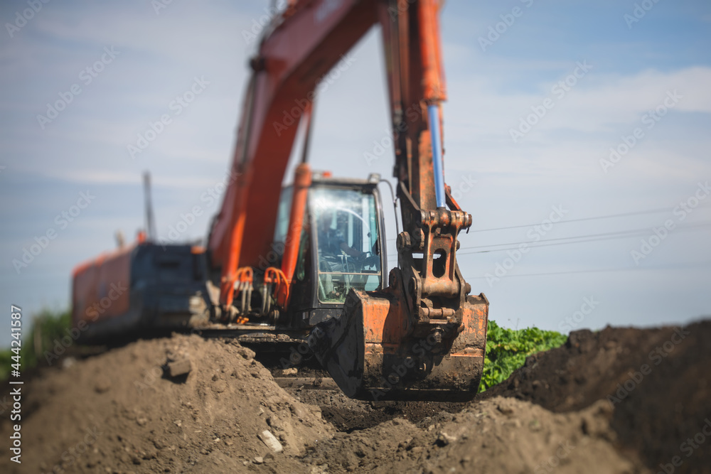 Yellow heavy excavator and bulldozer excavating sand and working during road works, unloading sand during construction of the new road