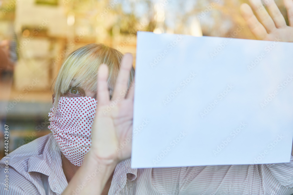 Senior woman in quarantine holds cry for help at window in case of