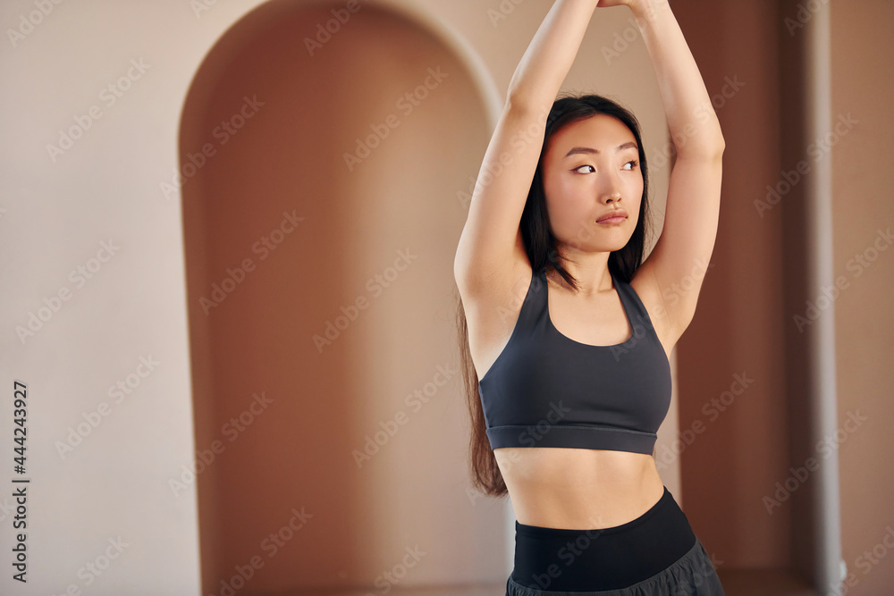 Doing fitness exercises. Young serious asian woman standing indoors
