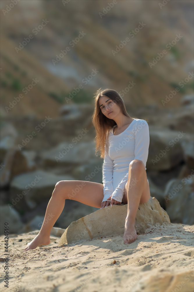 a young girl in a white bodysuit poses on a sandy platform among large stones