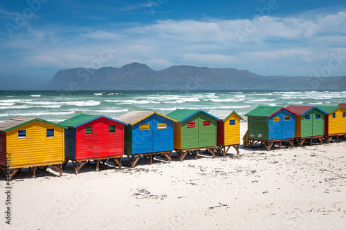 Famous colorful beach houses in Muizenberg near Cape Town, South Africa with mountains of Cape of Good Hope Peninsula in the background.