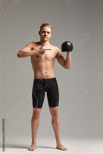 A swimmer, a young athlete in excellent physical shape, shows with his hand urging to start training, an advertising banner, a gray background, a copy of the space. © Georgii