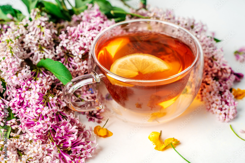 Fototapeta premium A mug of tea with lemon and lilac. Cozy romantic floral background with copy space. Flat lay.