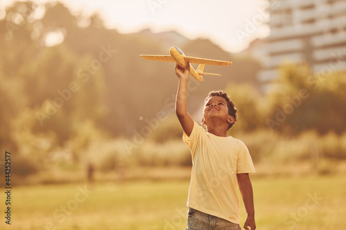 Playing with plane. African american kid have fun in the field at summer daytime