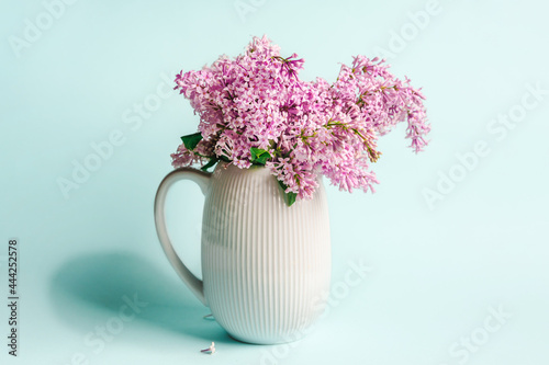 Beautiful floral composition on a blue background with a vase with lilac