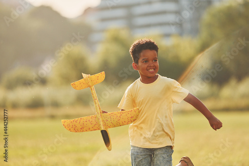 Playing with plane. African american kid have fun in the field at summer daytime