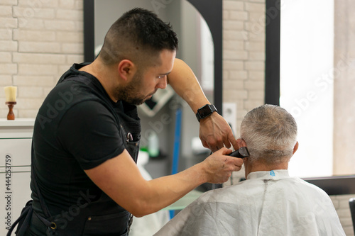 Barber cuts very concentrated hair of senior customer with cordless razor