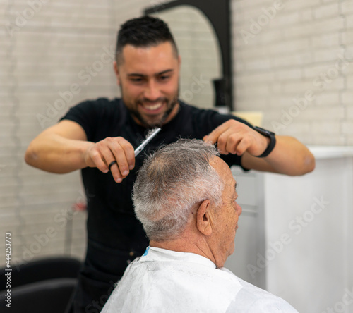 Barber enjoys cutting hair with scissors for senior client at barbershop