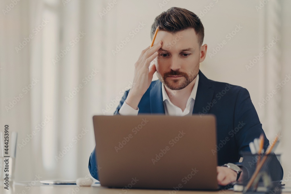 Thinking business executive sitting at his desk in front of laptop Thinking business executive sitting at his desk in front of laptop