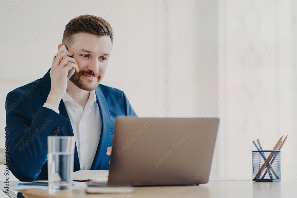 Young businessman talking on phone in front of laptop behind office desk Young businessman talking on phone in front of laptop behind office desk