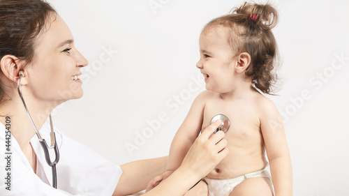 A pediatrician examines a baby girl who is one year old. The doctor uses a stethoscope to listen to the heartbeat of the chest. Smiling child looks at the doctor.
