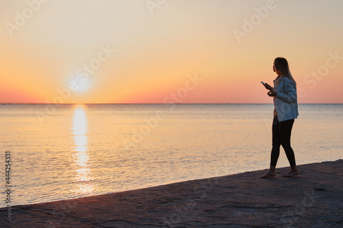 Beautiful girl stands by the sea and looks at the dawn. Girl in travel. Amazing scenic outdoors view. Beautiful dawn on the seashore. Adventure lifestyle