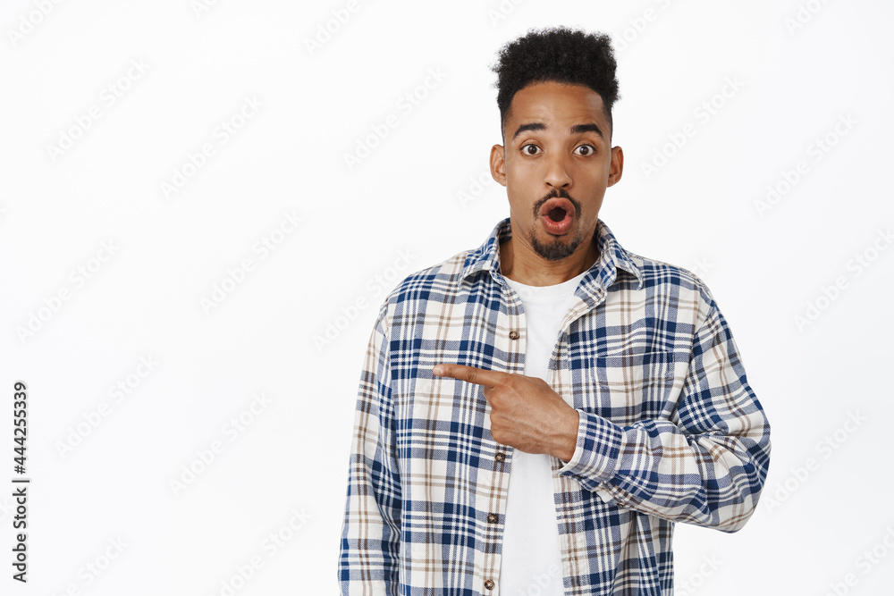 Surprised and amazed Black man pointing left at sale banner. Young african american guy gasp, say wow, showing advertisement on empty space, white background Surprised and amazed Black man pointing left at sale banner. Young african american guy gasp, say wow, showing advertisement on empty space, white background