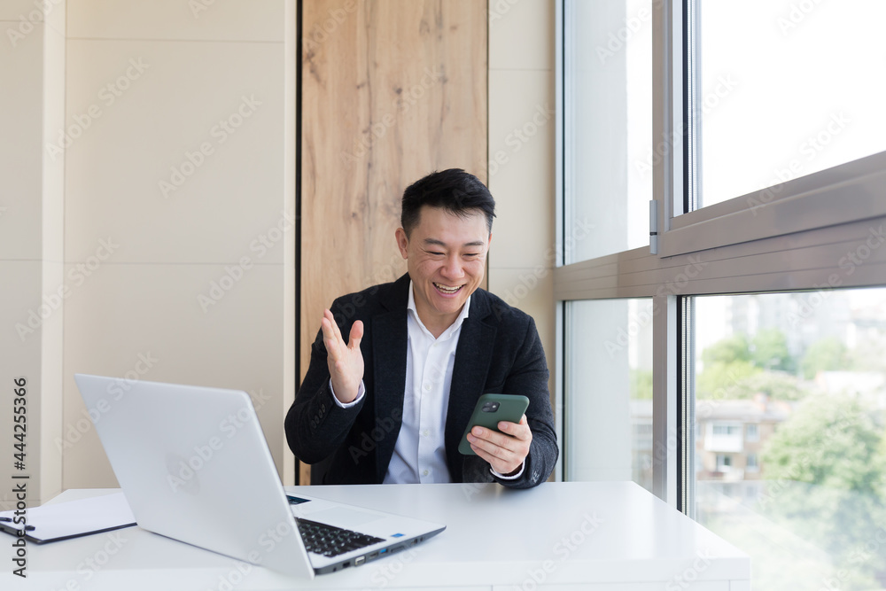 Happy young Asian business man in office looking at mobile phone, with emotion winner or win, financial stock sports betting. Male joyfully exclaims playing game. Excited overjoyed celebrating success Happy young Asian business man in office looking at mobile phone, with emotion winner or win, financial stock sports betting. Male joyfully exclaims playing game. Excited overjoyed celebrating success