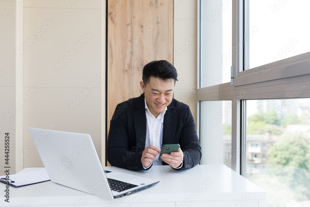 Happy young Asian business man in office looking at mobile phone, with emotion winner or win, financial stock sports betting. Male joyfully exclaims playing game. Excited overjoyed celebrating success Happy young Asian business man in office looking at mobile phone, with emotion winner or win, financial stock sports betting. Male joyfully exclaims playing game. Excited overjoyed celebrating success