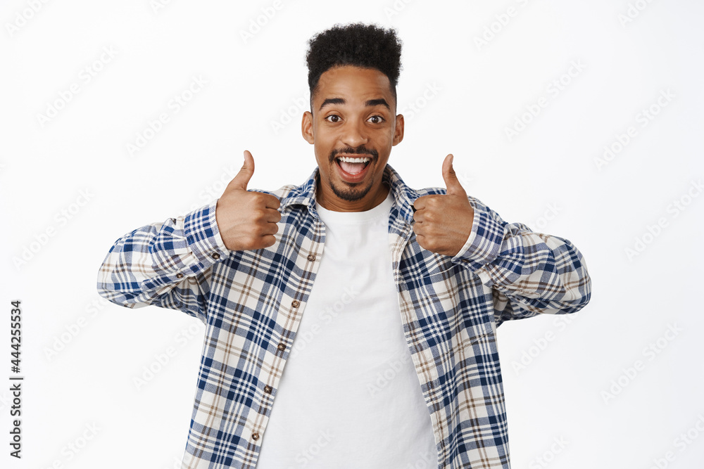 Cheerful young Black guy showing thumbs up. African american man like and approve smth good, praise great deal, recommend store or company, nod in approval say yes, white background Cheerful young Black guy showing thumbs up. African american man like and approve smth good, praise great deal, recommend store or company, nod in approval say yes, white background