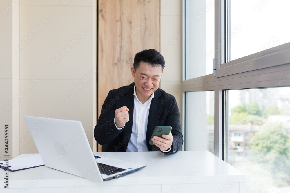 Happy young Asian business man in office looking at mobile phone, with emotion winner or win, financial stock sports betting. Male joyfully exclaims playing game. Excited overjoyed celebrating success Happy young Asian business man in office looking at mobile phone, with emotion winner or win, financial stock sports betting. Male joyfully exclaims playing game. Excited overjoyed celebrating success