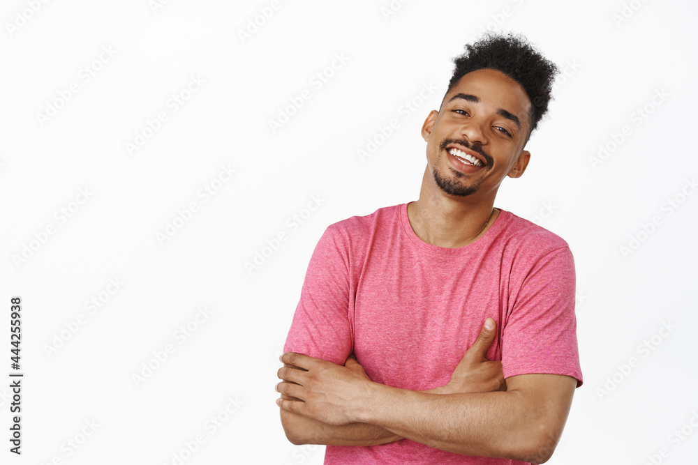 Lifestyle and people. Handsome african american man cross hands on chest, laughing and smiling with carefree expression, standing relaxed in pink casual t-shirt, white background Lifestyle and people. Handsome african american man cross hands on chest, laughing and smiling with carefree expression, standing relaxed in pink casual t-shirt, white background