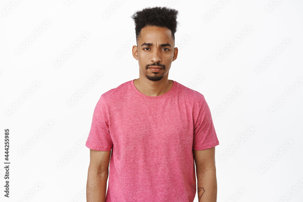 Sad and gloomy african american man furrow eyebrows, squinting and sulking with moody face expression, standing in pink t-shirt against white background Sad and gloomy african american man furrow eyebrows, squinting and sulking with moody face expression, standing in pink t-shirt against white background