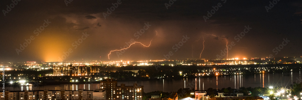 Night thunderstorm over the city. Night view of the city with the river, the sky is illuminated by lightning.
