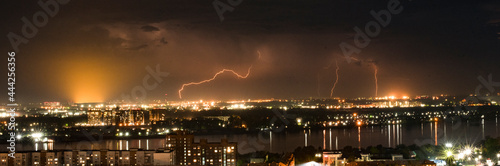 Night thunderstorm over the city. Night view of the city with the river, the sky is illuminated by lightning. 