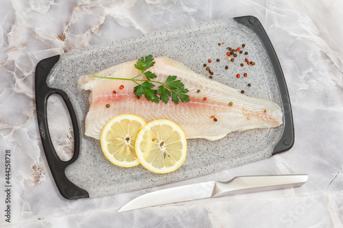 Fillet of raw pangasius fish with parsley leaves and lemon on cutting board