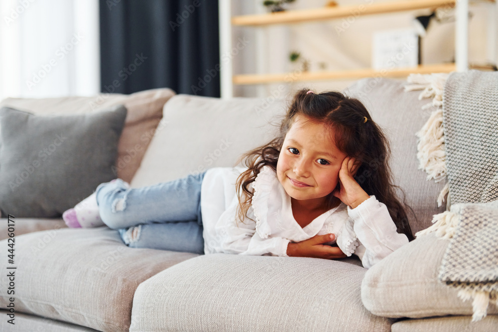 Laying down on the sofa. Little girl in casual clothes is at home alone Laying down on the sofa. Little girl in casual clothes is at home alone