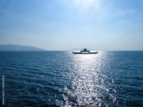 The dark silhouette of the ferry against the background of the reflection of the sun from the surface of the sea water