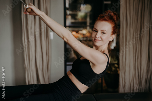 Young ginger female smiling while doing exercises on pilates reformer