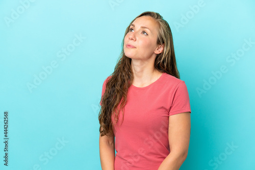 Young caucasian woman isolated on blue background looking to the side © luismolinero
