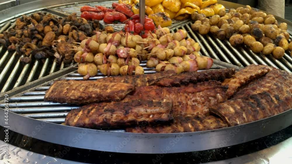 Preparation lamb or pork ribs, potato, mushrooms, bell peppers on large rotating grill on street market. Festival of street food. Close-up. Preparation lamb or pork ribs, potato, mushrooms, bell peppers on large rotating grill on street market. Festival of street food. Close-up.