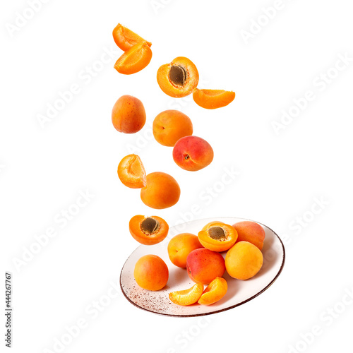 Fresh ripe whole and sliced apricot fruits falling on vintage plate isolated on white