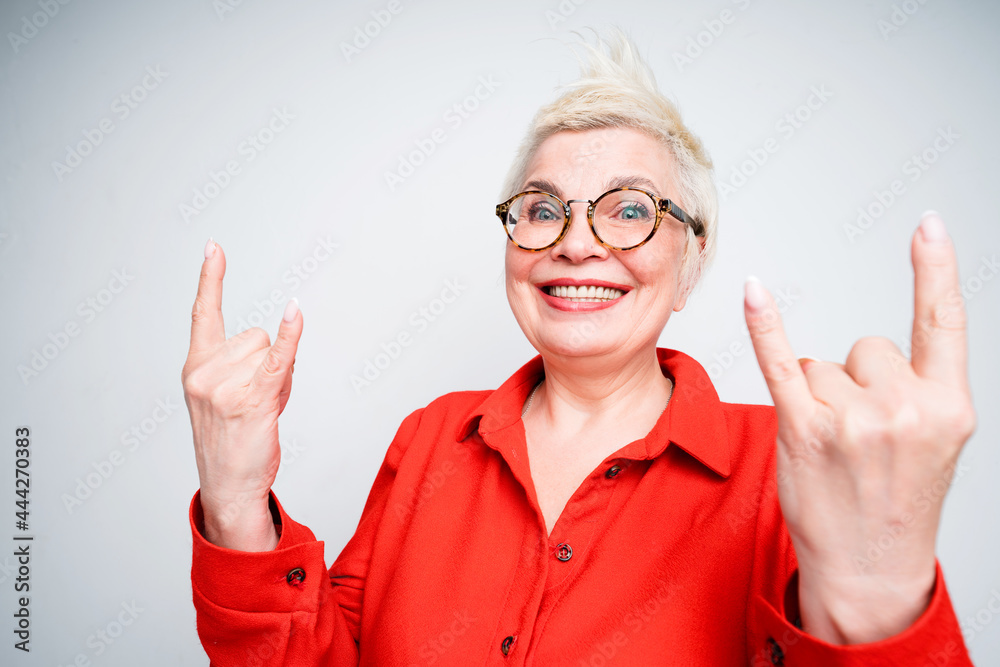 Cheerful elderly woman in glasses and with short hair shows the rock sign with her hands and smiles Cheerful elderly woman in glasses and with short hair shows the rock sign with her hands and smiles