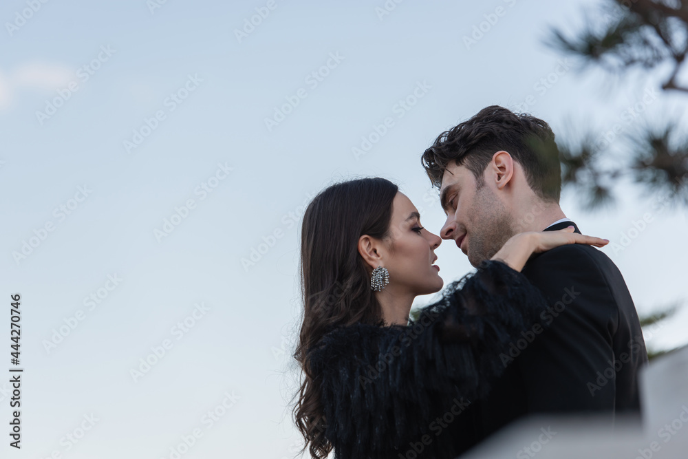 side view of man and woman in faux fur jacket hugging against blue sky side view of man and woman in faux fur jacket hugging against blue sky