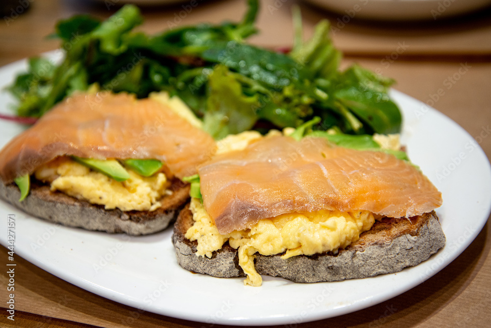 Scrambled eggs with fresh avocado and salmon served on two toasts  wheat bread with fresh lettuce on white plate for a healthy breakfast